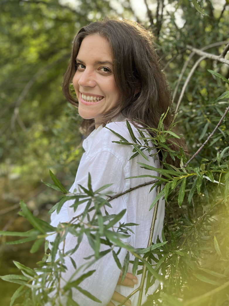 Picture of Sarah Hölzl, Coach for healthy Mindset, standing in a forest, surrounded by greens